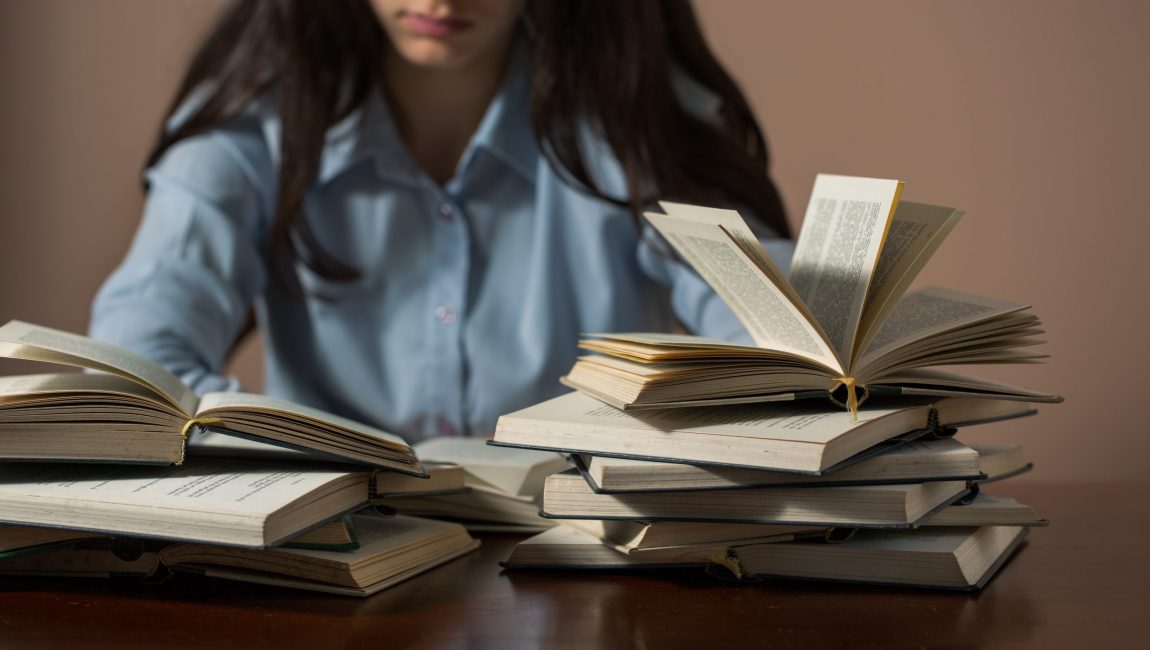 A teenage girl sitting at desk reading many books at home